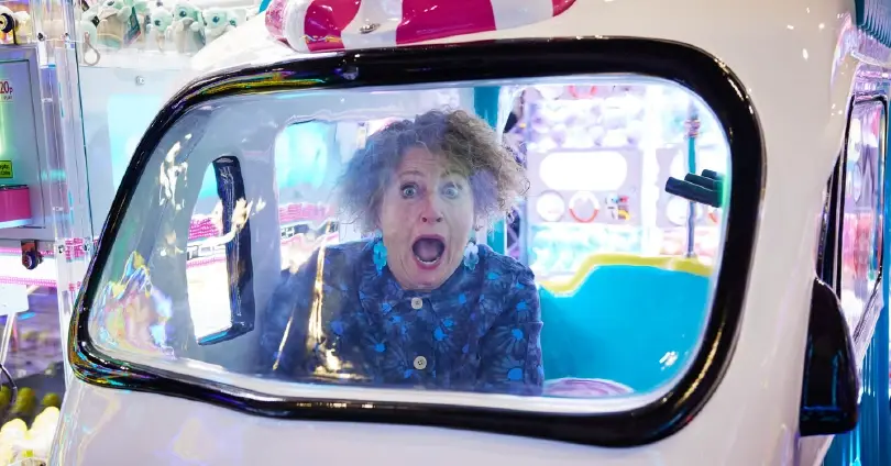 Woman with curly hair inside a colorful amusement ride capsule, mouth open in a surprised scream.